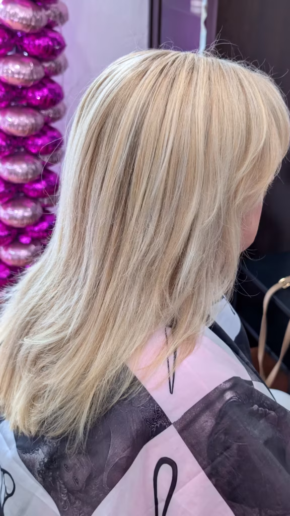 Długie, proste włosy blond z subtelnymi, jaśniejszymi pasemkami, które dodają fryzurze objętości i lekkości, wykonane w salonie Colors Premium.