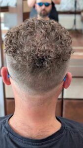 Widok od tyłu na męską fryzurę z trwałymi lokami i starannie wykonanym cieniowaniem (fade).