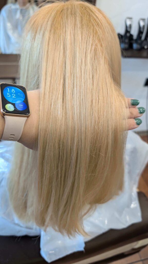 Zbliżenie na dłoń trzymającą pasmo idealnie gładkich, lśniących włosów w kolorze total blond, pokazujące ich doskonałą kondycję.