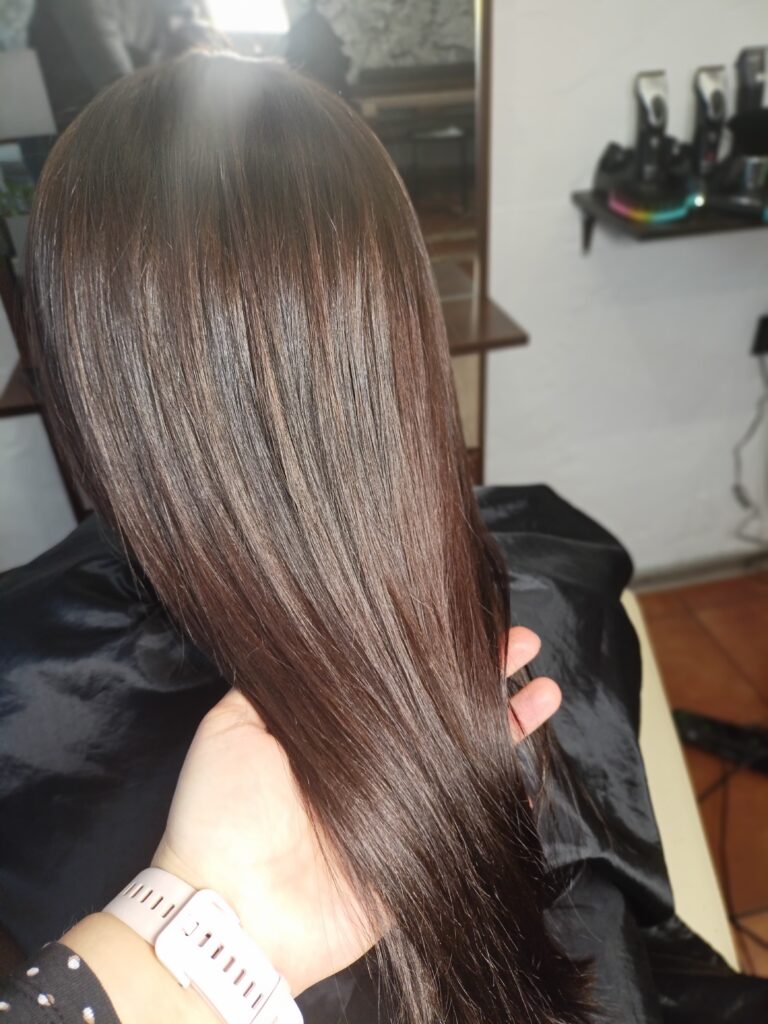 Stylista trzymający pasmo zdrowych, lśniących włosów w kolorze ciemnego brązu, by pokazać ich głęboki połysk po laminacji.