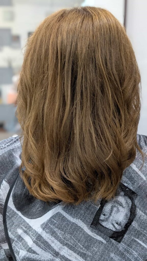 Długie, falowane włosy po zabiegu jednolitej koloryzacji na głęboki, lśniący brąz w salonie Colors Premium Słubice.