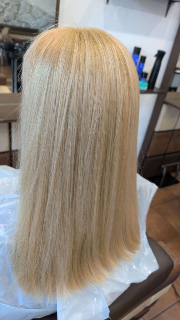 Widok od tyłu na długie, proste włosy w jednolitym kolorze total blond, lśniące zdrowym blaskiem po wizycie w naszym salonie w Słubicach.