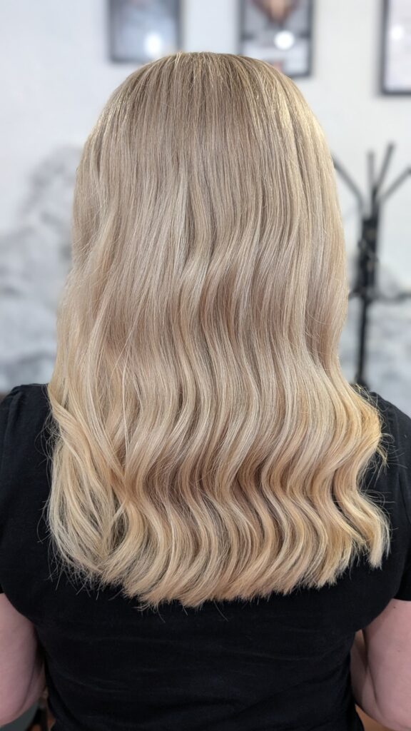 Średniej długości falowane włosy z naturalnym, słonecznym balayage, który nadaje fryzurze lekkości i efektu "muśnięcia słońcem".