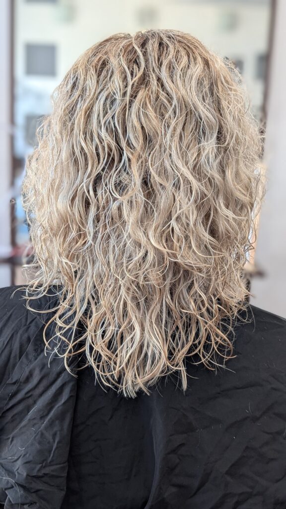 Długie, blond włosy po zabiegu stylizacji permanentnej, ułożone w naturalne, plażowe fale.