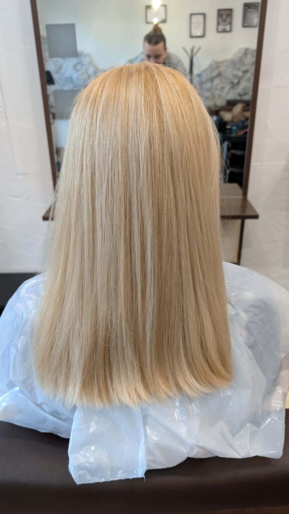 Długie włosy w kolorze total blond widziane od tyłu, odbijające się w lustrze, co podkreśla ich perfekcyjny stan i lustrzany blask.